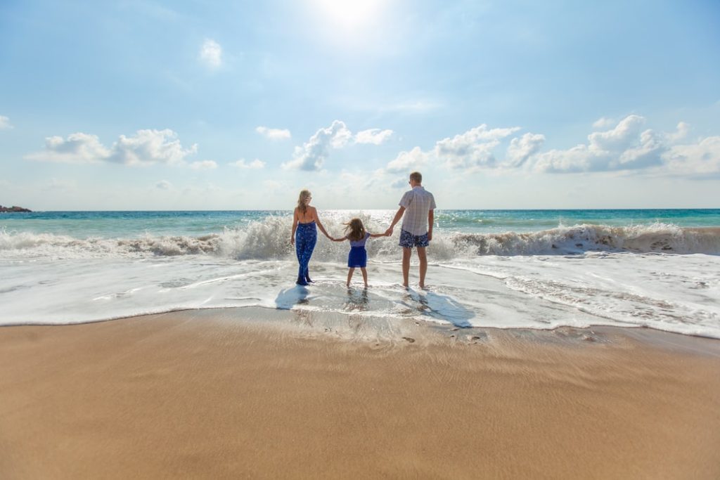 couple et une enfant au bord d'une plage, les pieds dans l'eau