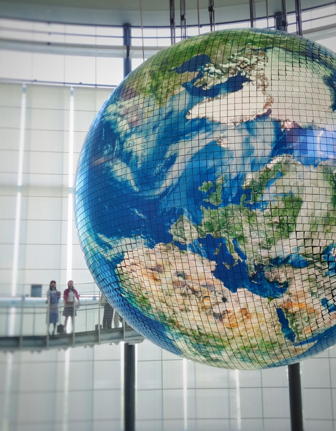 photographie de deux jeune femme regardant un immense globe terrestre suspendu et composé de petits cubes