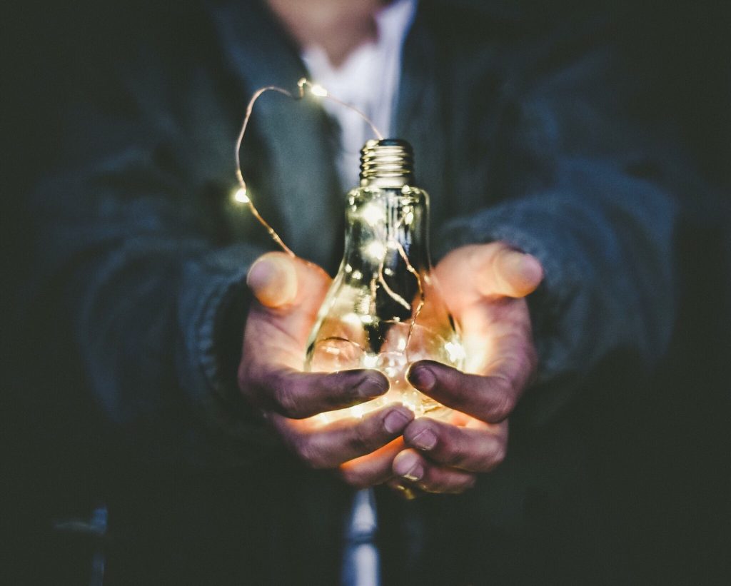 une ampoule avec une guirlande de lumière tenu au creux de deux mains