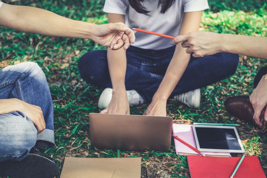 Team of young students studying in a group project in the park of university or school. Happy learning, community teamwork and youth friendship concept.