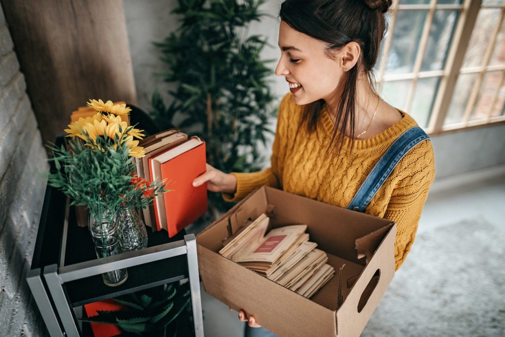 jeune femme déballant des livre d'un carton pour les mettre sur une étagère