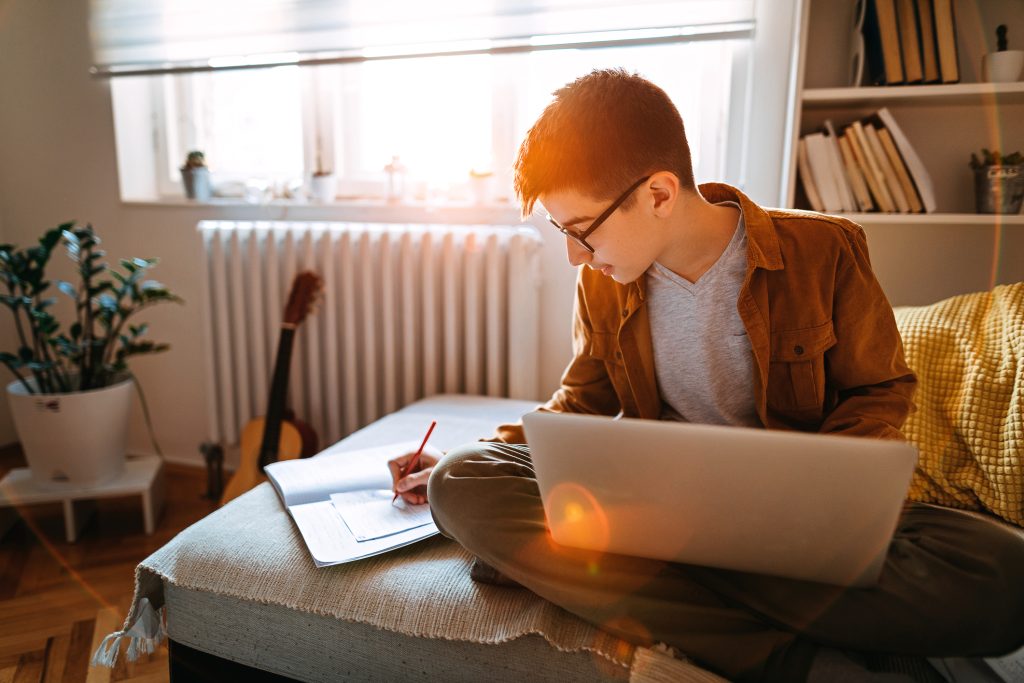 jeune étudiant faisant ses devoirs avec son pc et un carnet