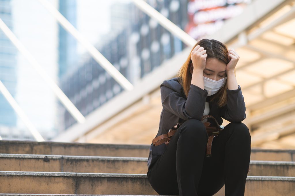 femme avec un masque covid se tenant la tête en étant assise sur des marches