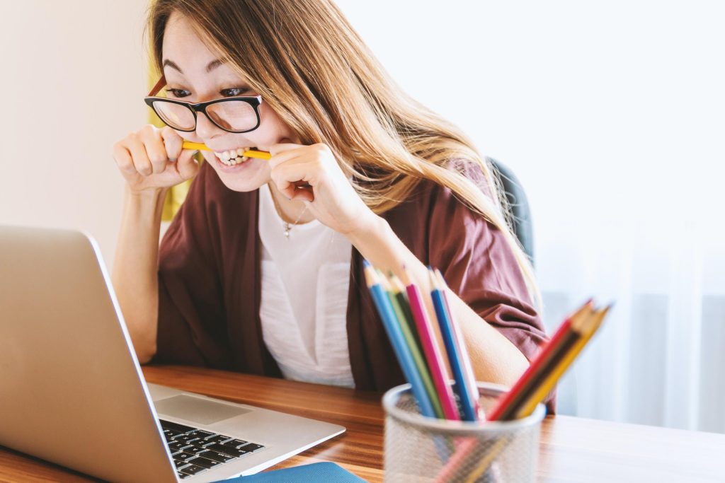 jeune femme mordant un crayon devant son écran de pc